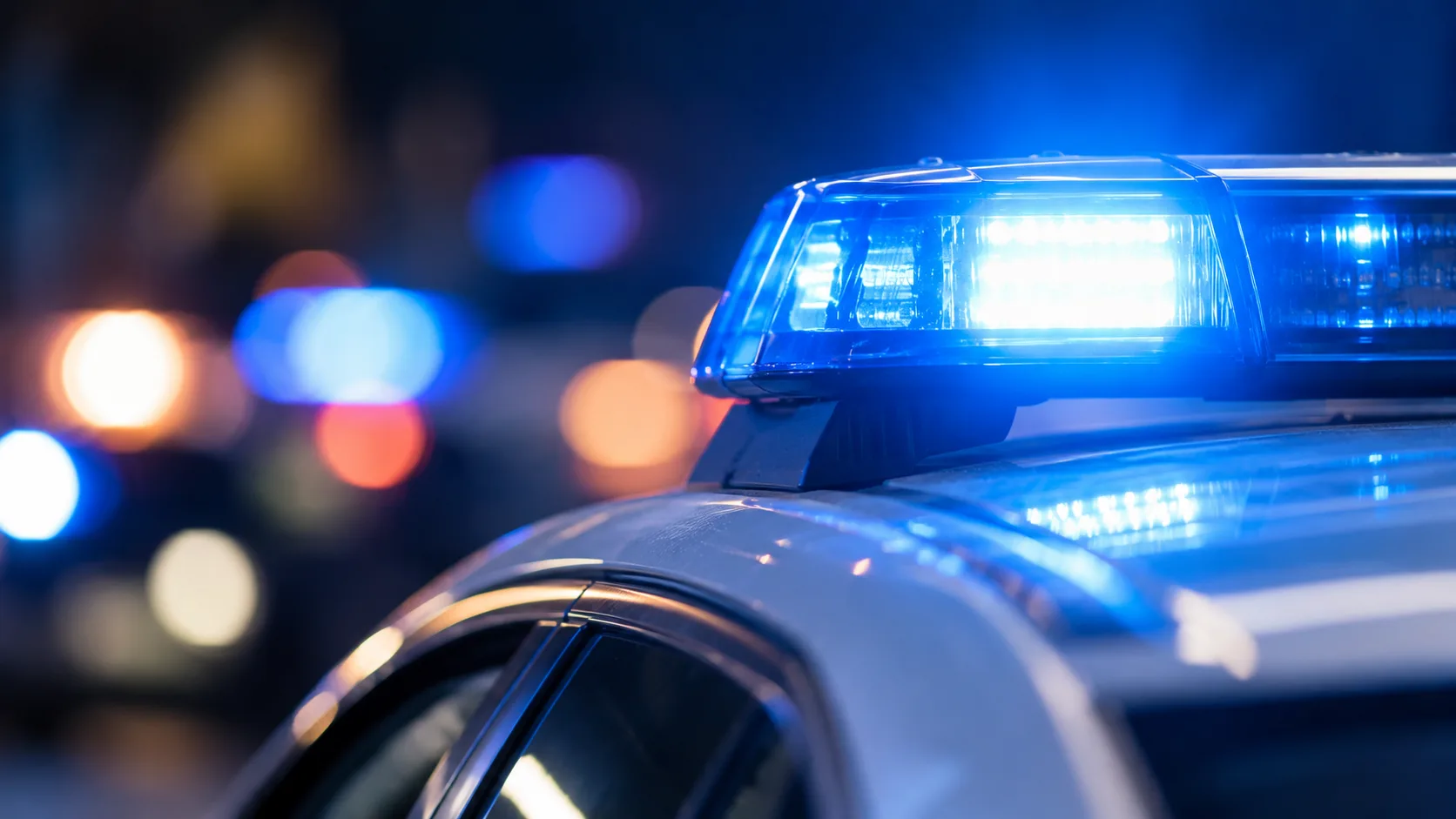 Blaues Warnlicht auf einem neutralen Polizeifahrzeug vor dunklem, unscharfem Hintergrund.