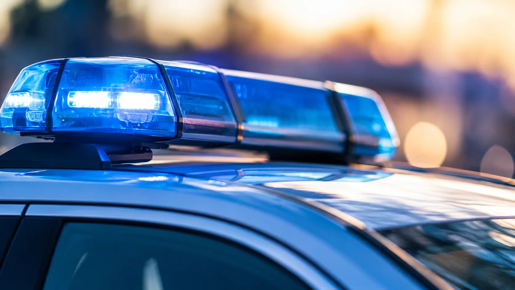 Blaues Polizeiblaulicht auf dem Dach eines neutralen Einsatzfahrzeugs vor unscharfem Hintergrund.