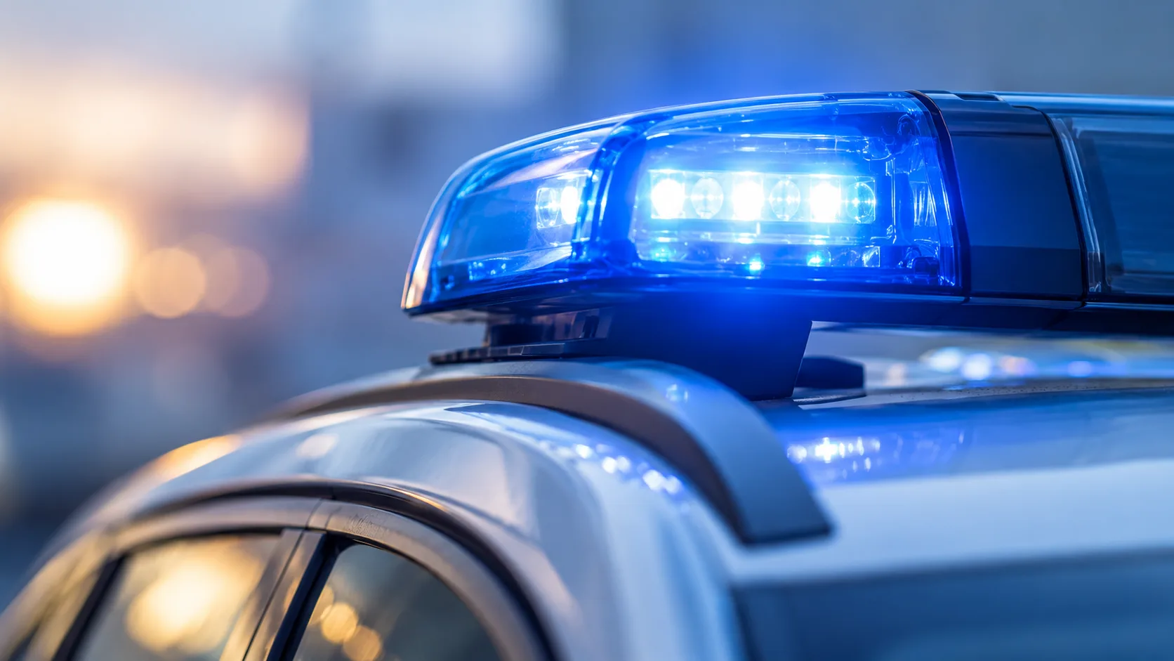 Blaues Rundumlicht auf dem Dach eines neutralen Polizeifahrzeugs vor unscharfem Hintergrund.