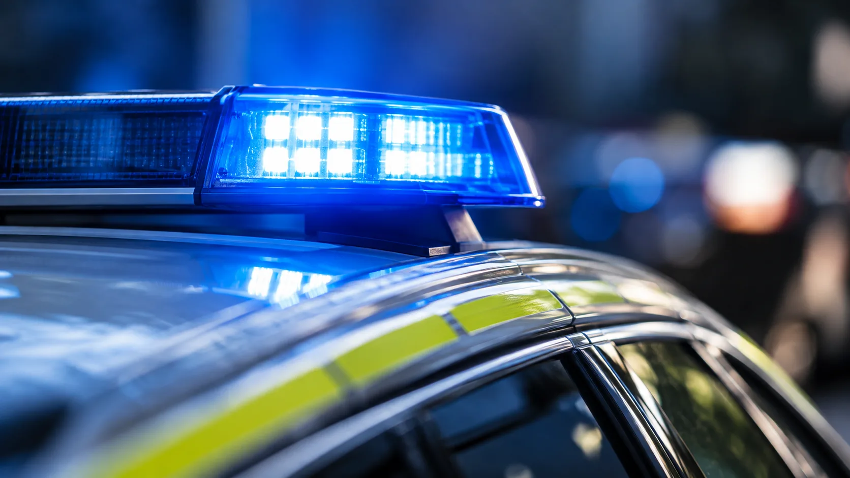 Neutrales Polizeifahrzeug mit Blaulicht vor dunklem, unscharfem Hintergrund ohne erkennbare Umgebung.