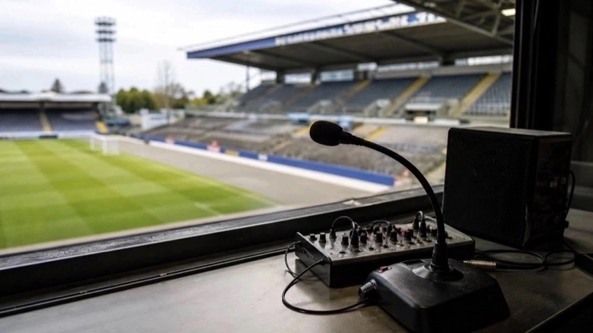 Leerer Sprecherplatz mit Mikrofon in einem Fußballstadion, unscharfes Spielfeld im Hintergrund, Regionalliga-Atmosphäre