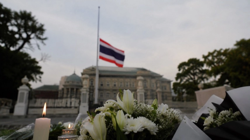 Flagge auf Halbmast vor einem anonymen Regierungsgebäude mit Blumen als Zeichen der Trauer in Thailand