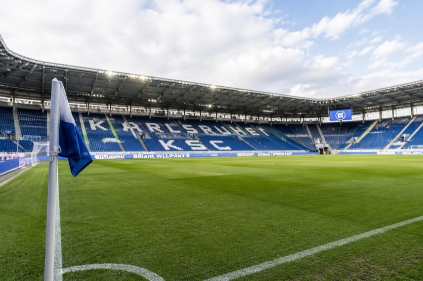 Leeres modernes Fußballstadion mit Rasen, Eckfahne und Tribünen bei Tageslicht.