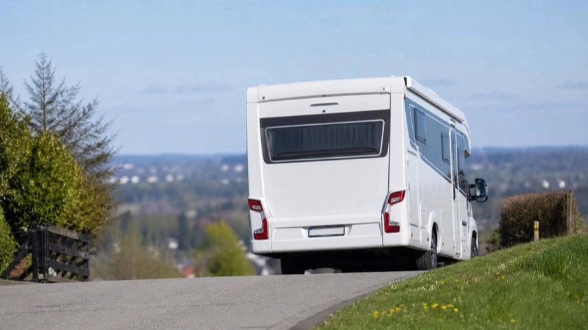 Wohnmobil steht auf abschüssiger Straße, Blick von hinten, Fahrzeug ohne Personen im Umfeld