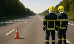 Zwei Feuerwehrleute mit Schutzkleidung und Helmen stehen auf einer leeren Autobahn und blicken in die Ferne Richtung Berlin.