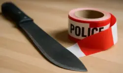 Nahaufnahme einer Machete neben rotem Polizeiband auf Holzfläche, illustrative Darstellung zum Polizeieinsatz in Köln-Bocklemünd.