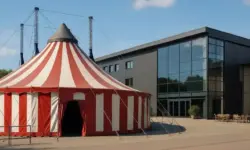 Zirkuszelt vor einem modernen Kulturgebäude als Darstellung des Kulturzentrums Tollhaus Karlsruhe.
