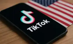 Smartphone mit TikTok-Logo vor unscharfer US-Flagge als Symbolbild für den geplanten Verkauf von TikTok in den USA.