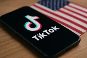Smartphone mit TikTok-Logo vor unscharfer US-Flagge als Symbolbild für den geplanten Verkauf von TikTok in den USA.