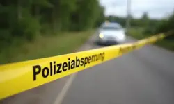 Polizeiabsperrung auf Landstraße mit gelbem Band und unscharfem weißen VW Golf im Hintergrund bei Tageslicht.