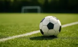 Ein schwarz-weißer Fußball liegt auf einem grünen Rasen mit einer weißen Spielfeldlinie im Vordergrund, im Hintergrund ist ein unscharfes Tor zu sehen.