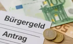Nahaufnahme von Eurobanknoten, Münzen und einem Formular mit der Aufschrift „Bürgergeld Antrag“ auf einem Holztisch.