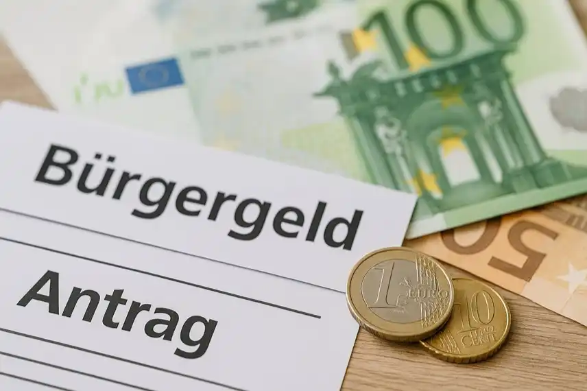 Nahaufnahme von Eurobanknoten, Münzen und einem Formular mit der Aufschrift „Bürgergeld Antrag“ auf einem Holztisch.