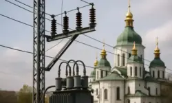 Ein Strommast mit Transformator und Leitungen im Vordergrund, im Hintergrund eine Kirche mit grünen Kuppeln und goldenen Türmen in Kiew.