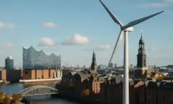 Windrad im Vordergrund mit Blick auf Hamburgs Innenstadt, die Elbphilharmonie und historische Backsteinbauten bei sonnigem Wetter.