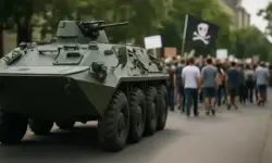 Ein grünes Militärfahrzeug steht auf einer Straße vor einer Gruppe von Demonstrierenden mit Plakaten.