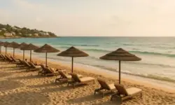 Sonniger Mittelmeerstrand mit Liegen und Strohdächern bei ruhiger See und goldener Abendstimmung.