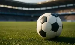 Ein schwarz-weißer Fußball liegt auf grünem Rasen in einem Stadion bei warmem Sonnenlicht.