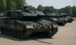 Mehrere moderne deutsche Kampfpanzer in Tarnfarben stehen auf einem Betonplatz bei Tageslicht, im Hintergrund weitere Panzer leicht unscharf.