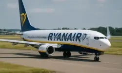 Ein Passagierflugzeug steht auf dem Rollfeld eines Flughafens bei Tageslicht, im Hintergrund Wiesen und Himmel mit leichten Wolken.