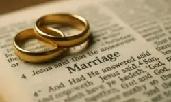 Zwei ineinanderliegende goldene Ringe liegen auf einer geöffneten Bibel, im Fokus steht das Wort „Marriage“.