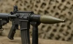 Nahaufnahme eines schwarzen Sturmgewehrs mit Granataufsatz vor einem unscharfen Tarnhintergrund.