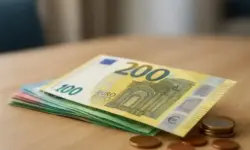 Ein Stapel verschiedener Euro-Banknoten und Münzen liegt auf einer Holzoberfläche, im Hintergrund unscharf ein heller Raum.