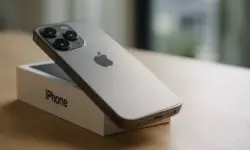 Ein silbernes iPhone liegt schräg auf einer weißen Box auf einem Holztisch, im Hintergrund ein heller Raum mit unscharfer Tiefe.