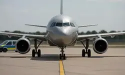 Ein silbernes Passagierflugzeug steht auf dem Rollfeld, im Hintergrund ein Polizeifahrzeug bei klarem Tageslicht.