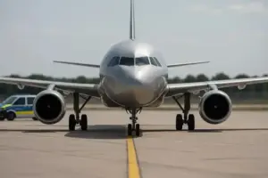 Ein silbernes Passagierflugzeug steht auf dem Rollfeld, im Hintergrund ein Polizeifahrzeug bei klarem Tageslicht.