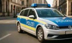 Deutsches Polizeiauto mit blauer und gelber Beschriftung „Polizei“, geparkt auf einer sonnigen Stadtstraße mit Gebäuden im Hintergrund.