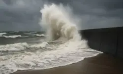 Hohe Wellen schlagen bei Sturm gegen eine Küstenmauer unter dunklen Wolken.