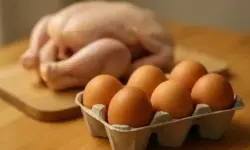 Ein Karton mit braunen Eiern im Vordergrund, dahinter unscharf ein rohes Huhn auf einem Holzbrett.