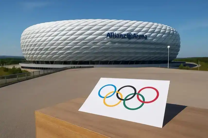 Die Allianz Arena in München bei Tageslicht, im Vordergrund ein Blatt Papier mit den fünf olympischen Ringen auf einem Tisch.