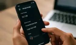 Nahaufnahme einer Hand, die auf einem Smartphone die WhatsApp-Funktion „Speicher verwalten“ im Chat-Info-Bereich öffnet, im Hintergrund ein Laptop auf einem Tisch.