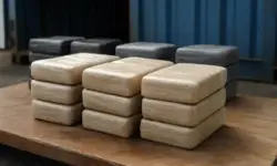 Mehrere gestapelte, in Plastikfolie verpackte Pakete auf einer Holzfläche vor einem blauen Container.