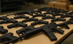 Mehrere schwarze Schusswaffen, darunter Gewehre und Pistolen, liegen ordentlich auf einem Holztisch in einem hell beleuchteten Raum.