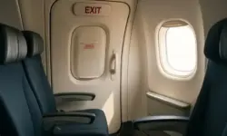 Innenansicht eines Flugzeugs mit Sitzreihe und geschlossener Notausgangstür, durch ein Fenster fällt helles Tageslicht.