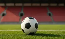 Nahaufnahme eines Fußballes auf grünem Rasen in einem leeren Stadion mit roten Sitzreihen im Hintergrund.