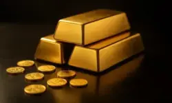 Ein Stapel glänzender Goldbarren liegt auf einem dunklen, reflektierenden Untergrund, daneben sind einige verstreute Goldmünzen zu sehen.