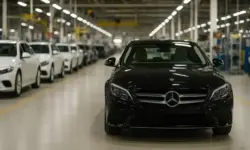 Ein schwarzer Mercedes steht in einer Produktionshalle mit weiteren Fahrzeugen im Hintergrund.