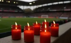Rote brennende Kerzen in Glasbehältern am Spielfeldrand eines Fußballstadions mit unscharfem Hintergrund aus Zuschauern und Spielfeld.
