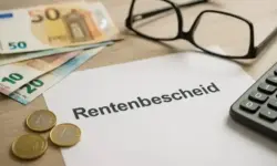 Ein Rentenbescheid liegt auf einem Holztisch, daneben Euro-Geldscheine, Münzen, eine Brille und ein Taschenrechner.