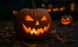 Leuchtender geschnitzter Kürbis mit Kerze auf Holzuntergrund, umgeben von Herbstblättern, im Hintergrund unscharf weitere beleuchtete Kürbisse.
