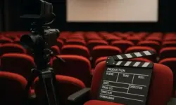 Professionelle Filmkamera auf Stativ und Filmklappe in einem leeren Kinosaal mit roten Sitzen.