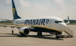 Ein Passagierflugzeug steht auf dem Rollfeld bei Sonnenschein, mit Bodenpersonal und geöffneter Treppe im Hintergrund.