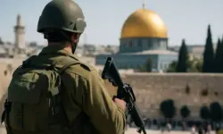 Israelischer Soldat in Uniform steht mit Gewehr vor dem Felsendom in Jerusalem, im Hintergrund verschwommene Stadtansicht bei Tageslicht.