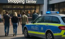 Polizeiauto steht vor einem modernen Einkaufszentrum, mehrere Menschen gehen in Richtung Eingang.