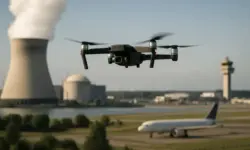 Drohne im Flug über einem Atomkraftwerk mit Kühltürmen und einem Flughafen im Hintergrund bei Tageslicht.