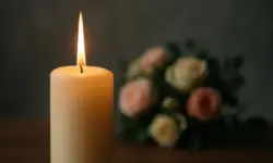 Eine einzelne brennende Kerze vor einem unscharfen Hintergrund mit Blumen.